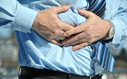 Ein Mann fasst sich an den Bauch, weil er Schmerzen hat. Ein Mann fasst sich an den Bauch, weil er Schmerzen hat.