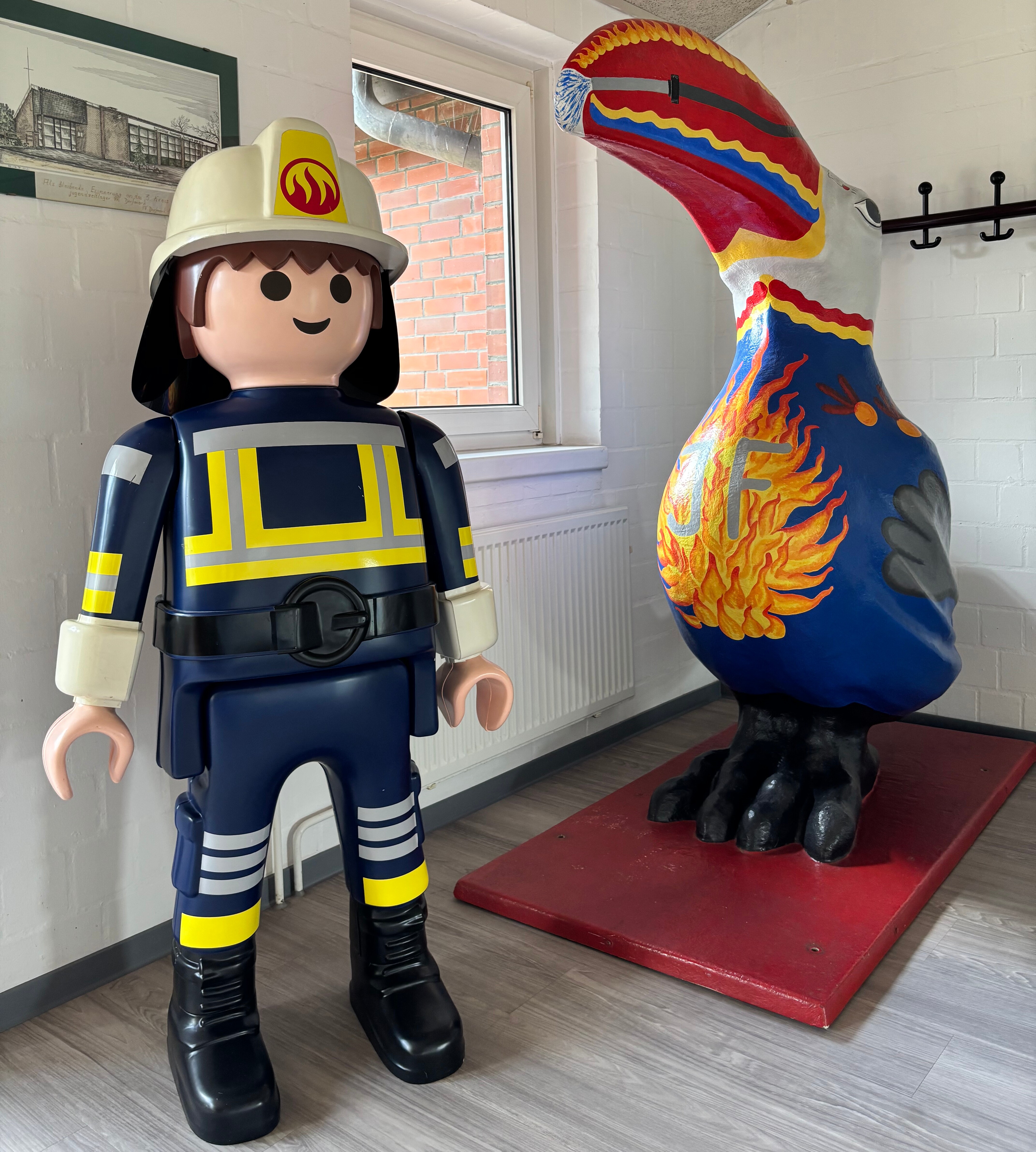 Eine große Playmobilperson ist als Feuerwehrmann gekleidet und daneben steht ein großer Tukan.