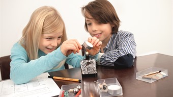 zwei Kinder experimentieren mit Batterie, Glühbirne und Teelicht