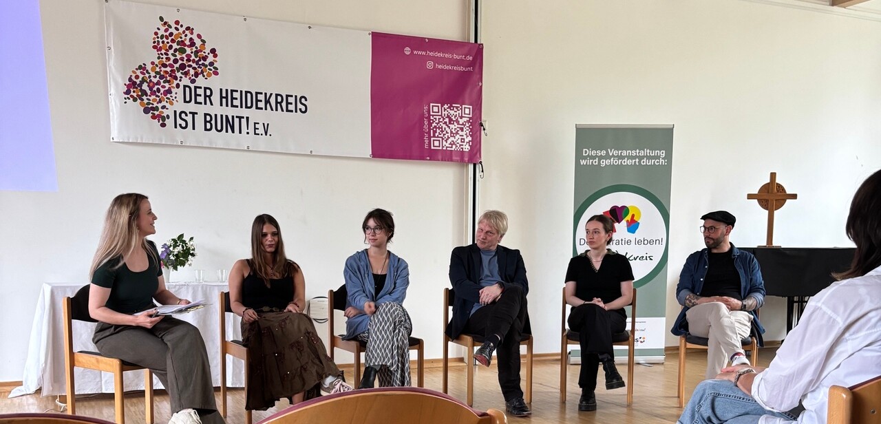 Eine Personengruppe sitzt vor einem Publikum Eine Personengruppe sitzt vor einem Publikum