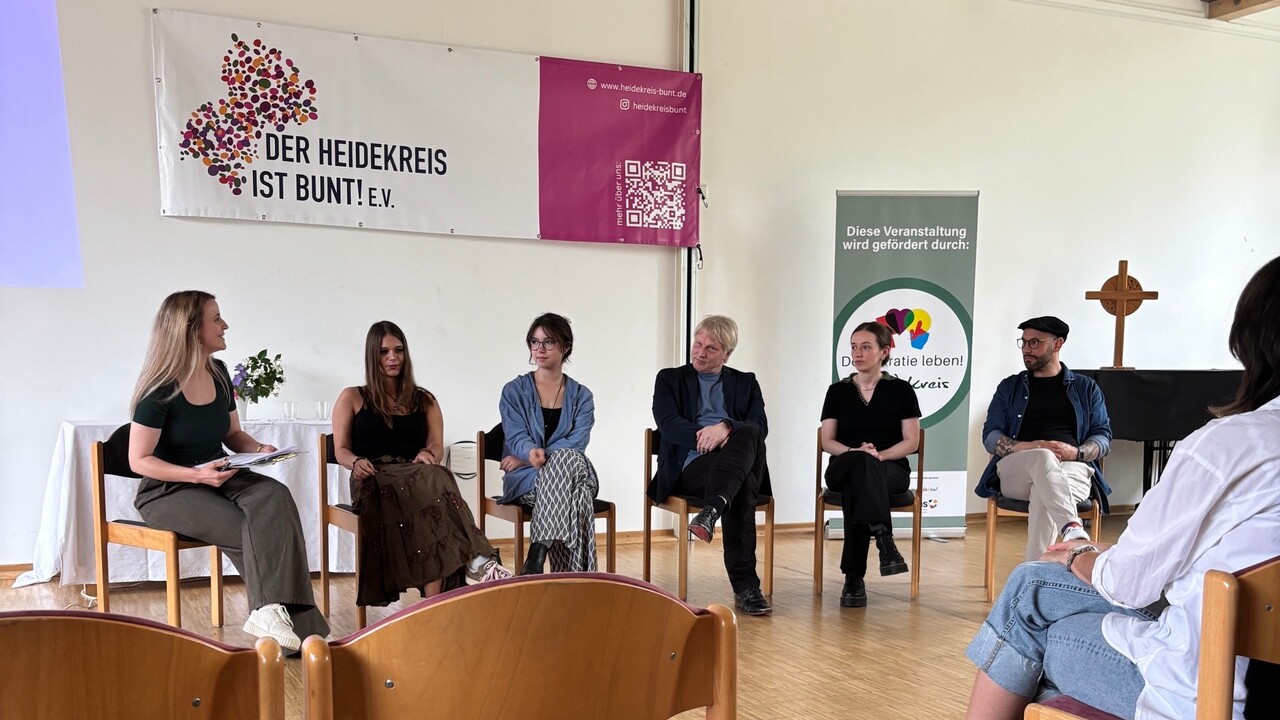 Eine Personengruppe sitzt vor einem Publikum Eine Personengruppe sitzt vor einem Publikum