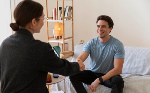 Eine junge Frau gibt einem jungen Mann die Hand. Sie befinden sich in einer Wohnung.