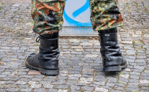 Eine Person in Bundeswehrstiefeln steht auf Kopfsteinplaster. Eine Person in Bundeswehrstiefeln steht auf Kopfsteinplaster.
