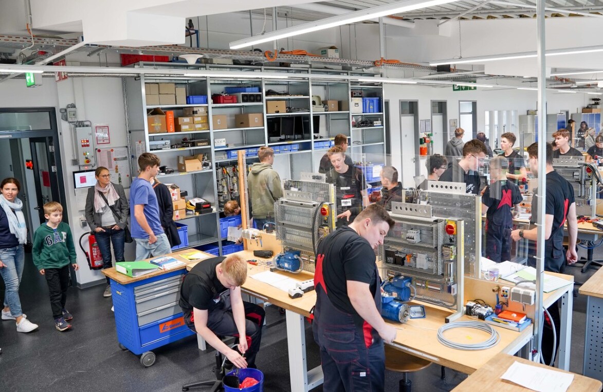 In einer Werkzeughalle sind Beschäftigte mit jungen Menschen, die sich über die verschiedenen Berufe austauschen.