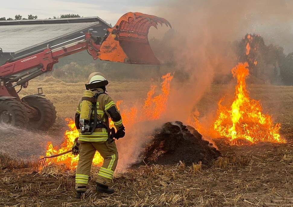 Ein Feld brennt. Ein Feuerwehrmann löscht.