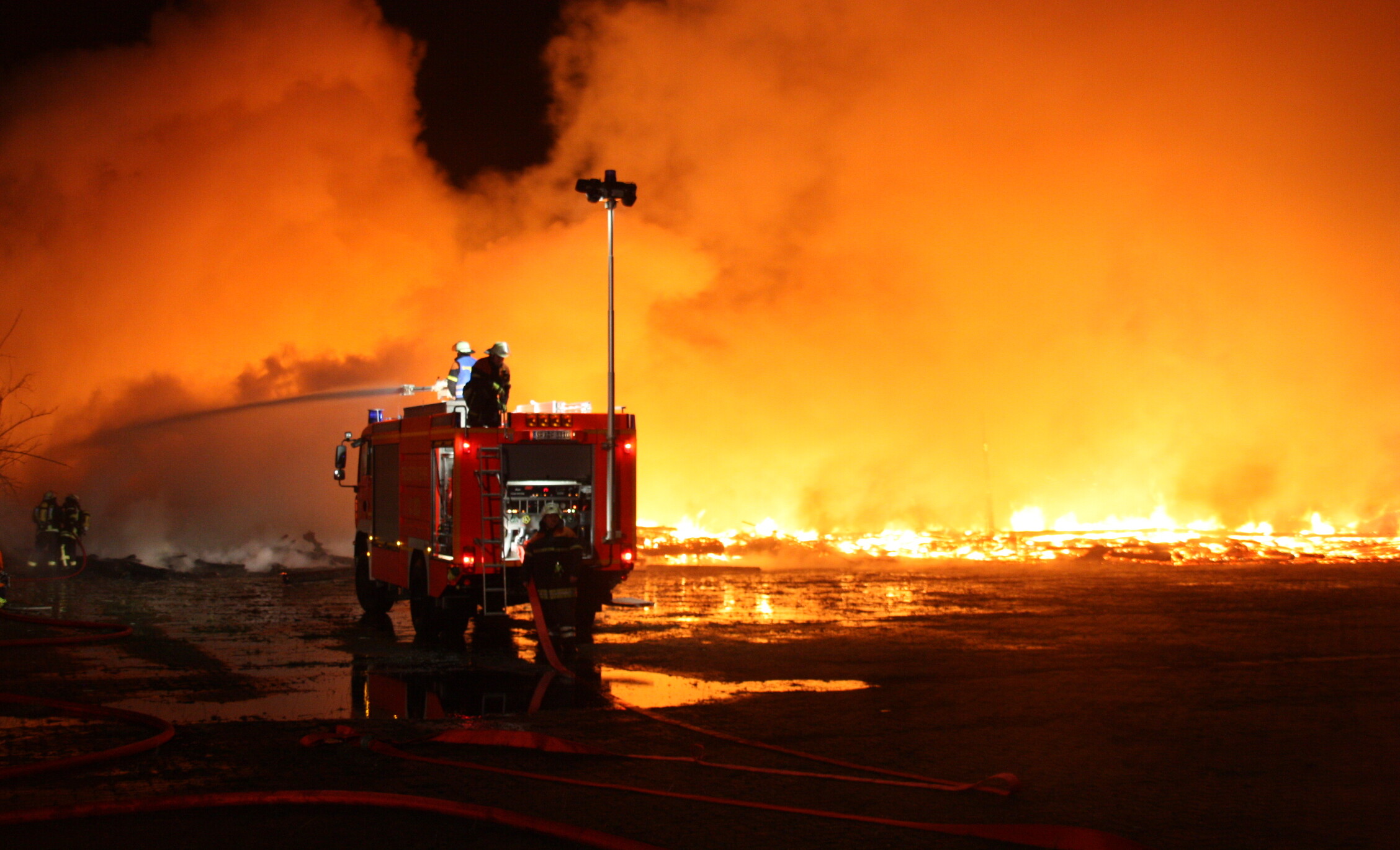 Ein Feuerwehrfahrzeug steht vor einem sehr großem Feuer.