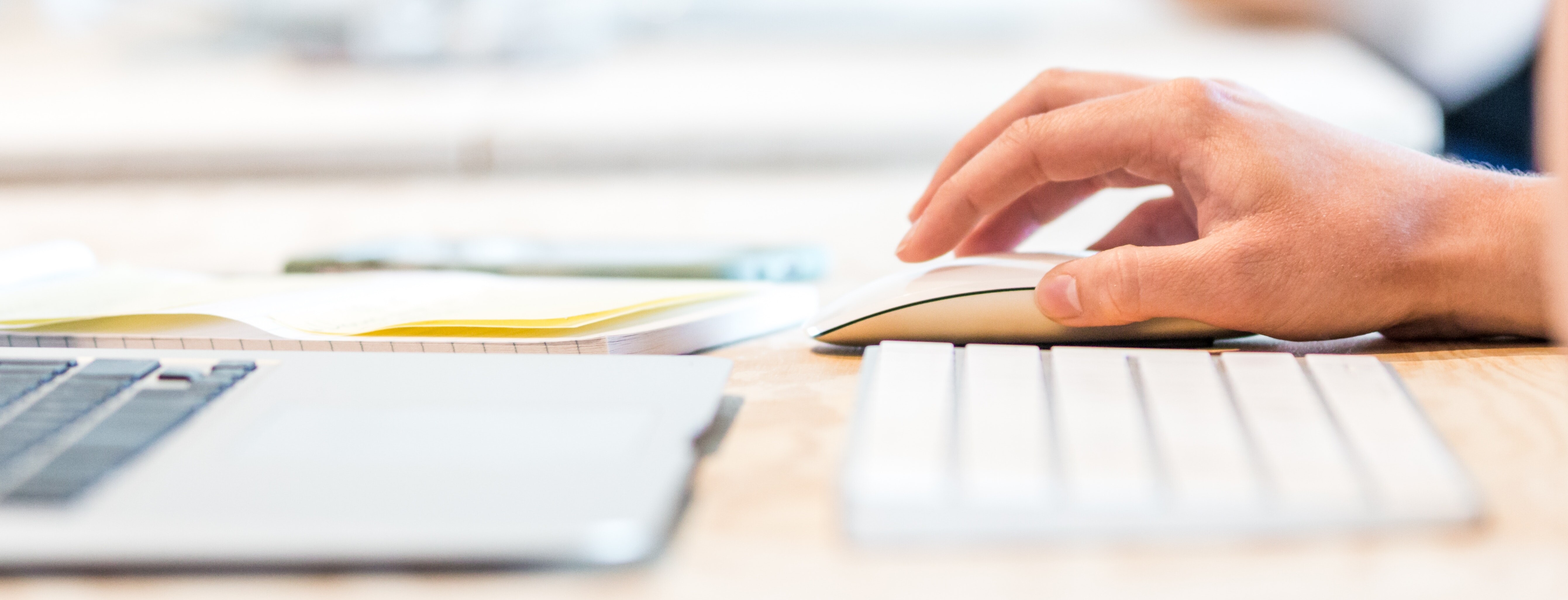 Eine Person arbeite mit einer Maus am Bildschirm und macht sich auf Papier Notizen.