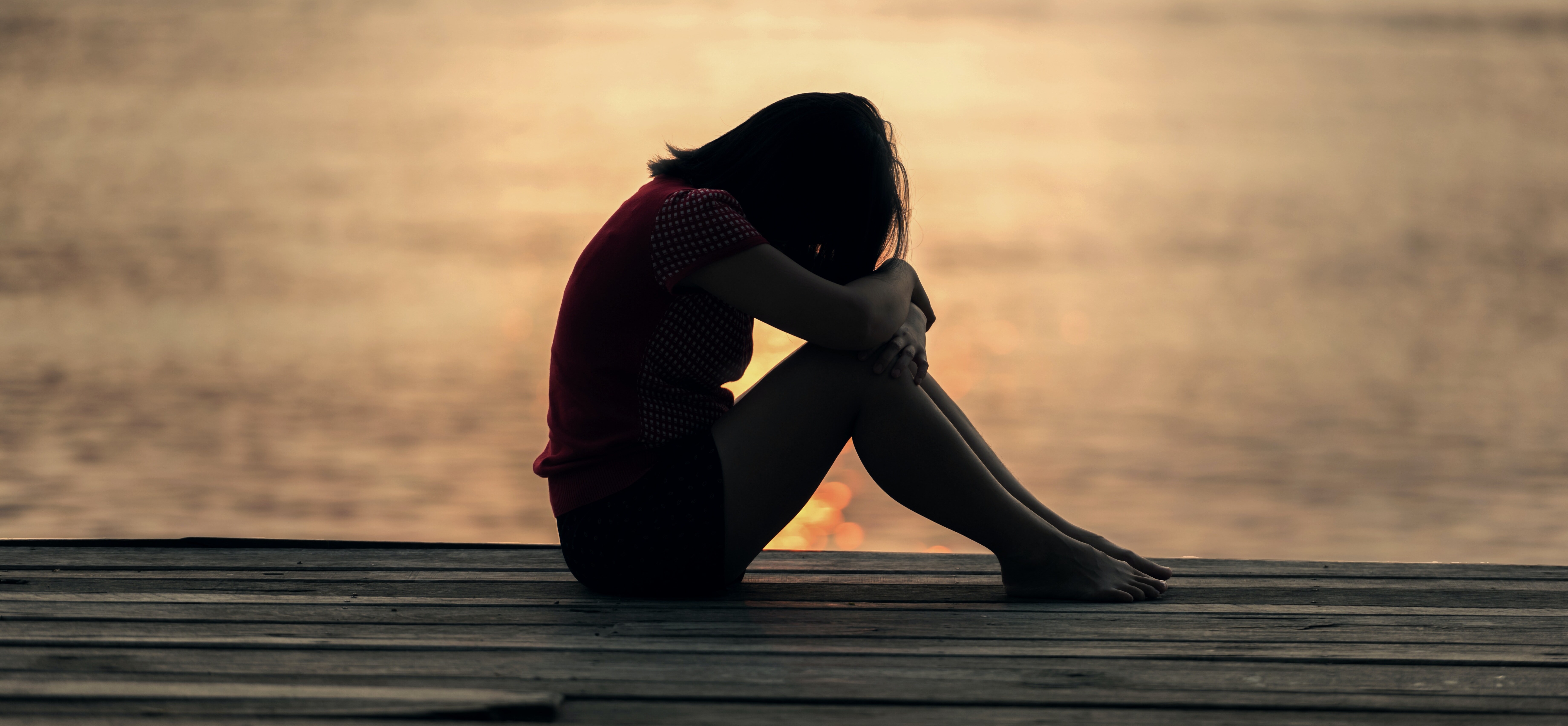 Eine Frau sitzt zusammengezogen im Sonnenuntergang. 