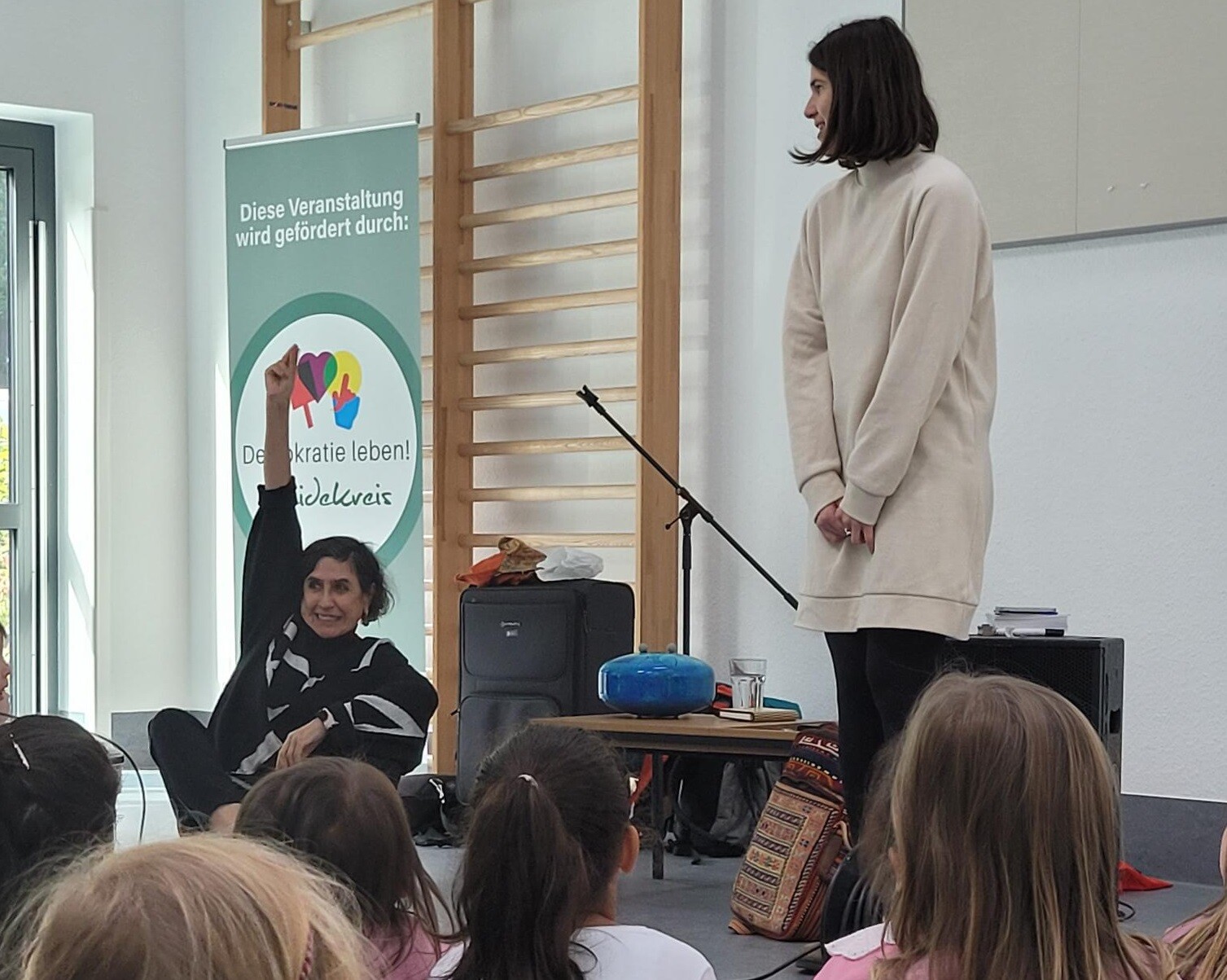 Kinder sitzen auf Matten und hören den Darstellern zu. 