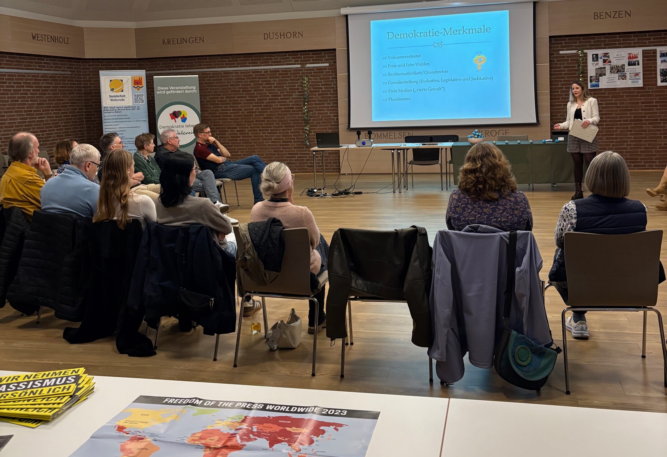 Gäste sitzen im Halbkreis und hören zu. 