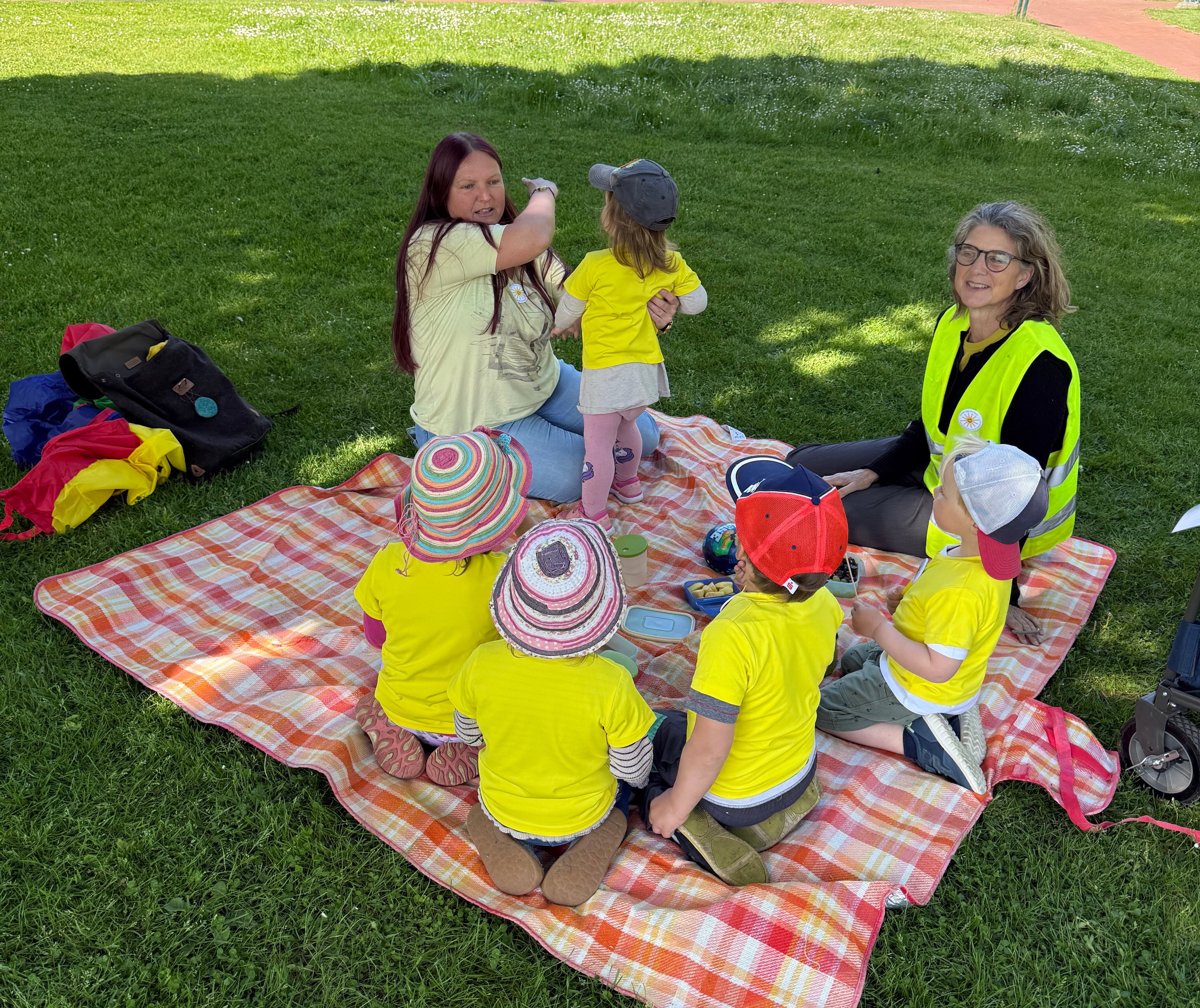 Kinder und Erwachsene sind in Geldb gekleidet und sitzen auf einer Picknickdecke. Kinder und Erwachsene sind in Geldb gekleidet und sitzen auf einer Picknickdecke.