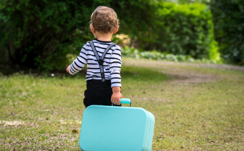 Ein Kind zieh einen kleinen Koffer hinter sich her. 