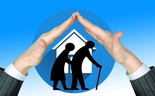 Zwei Hände rahmen ein Haus mit zwei älteren Menschen ein.