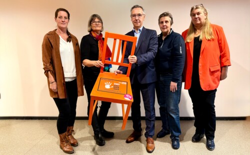 Gleichstellungsbeauftragte und der Landrat präsentieren einen Stuhl in der Farbe Orange. Gleichstellungsbeauftragte und der Landrat präsentieren einen Stuhl in der Farbe Orange.